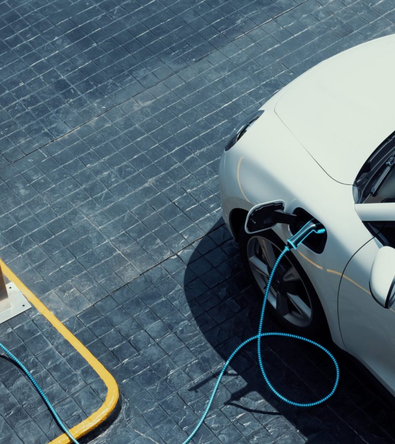 Aerial view electric car recharging battery from EV charging station at city center public car park. Future innovative rechargeable EV car using alternative clean and sustainable energy. Peruse